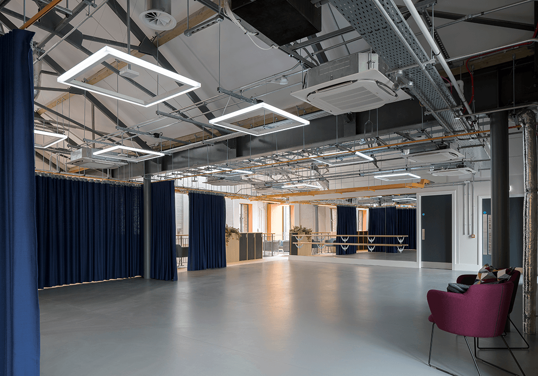 Large open event space featuring a mirrored wall with a ballet barre attached, curtains for sectioning the space and chairs.