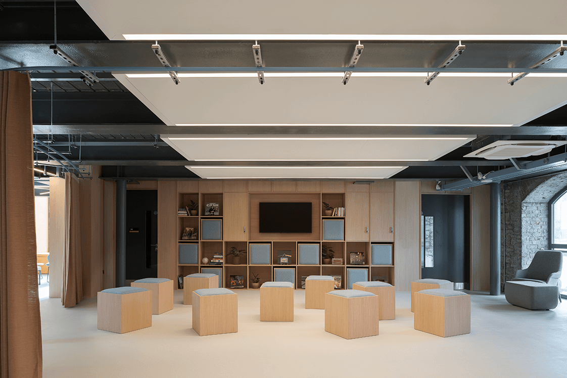 Half of the Encore event space with 10 cushioned wooden stools, an armchair and a presentation screen.